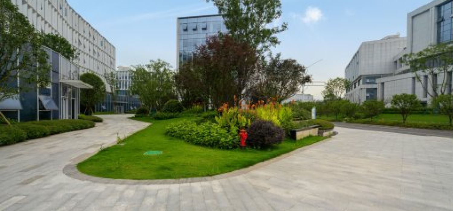 Area verde curata con aiuole fiorite e alberi al centro di un complesso di edifici moderni a uso ufficio o industriale