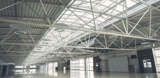 Interno di un grande spazio commerciale o fieristico vuoto con soffitto a tralicci metallici e ampie vetrate che diffondono luce naturale