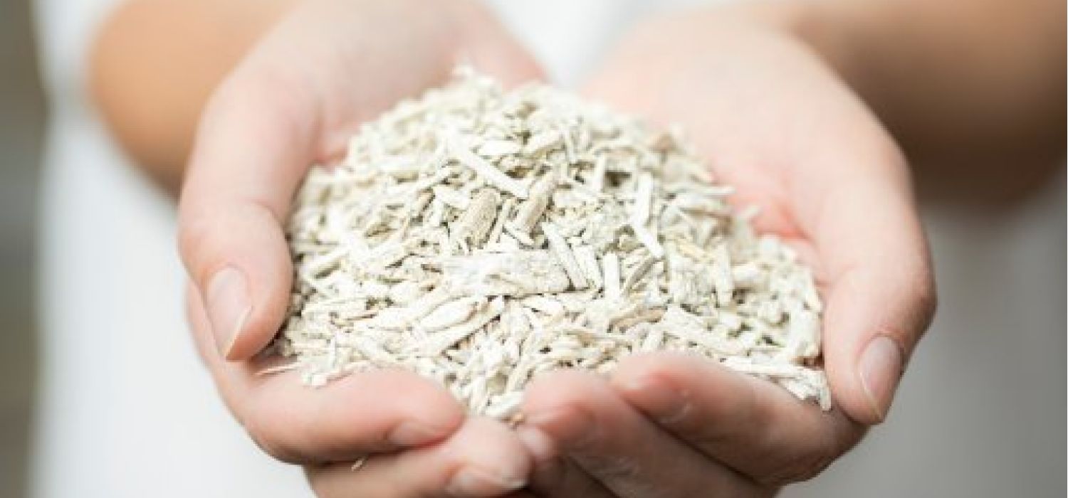 Mani che reggono una manciata di fibra minerale o materiale isolante sfuso di colore grigio-bianco