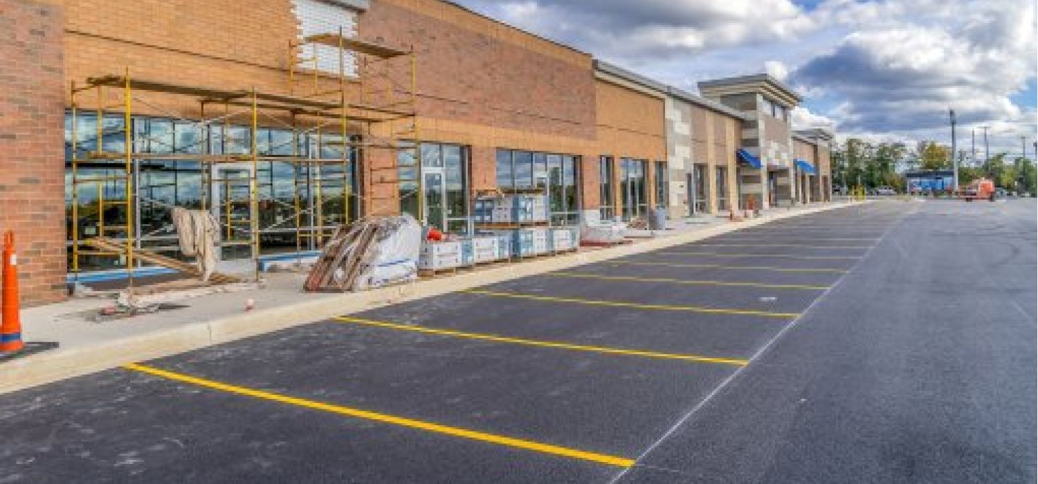 Centro commerciale in costruzione con ponteggi sulla facciata in mattoni, parcheggio asfaltato appena completato e materiali edili sul marciapiede