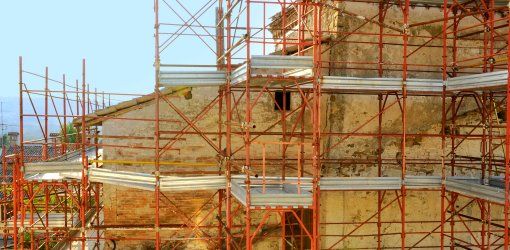 RESTAURO CONSERVATIVO: VALORIZZARE IL PASSATO NELL'EDILIZIA MODERNA 1 Ponteggio metallico rosso a più livelli attorno alla facciata in pietra di un edificio storico in fase di restauro