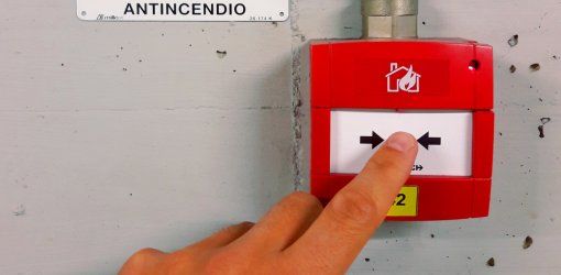 Mano che preme un pulsante di allarme antincendio rosso a parete con targa identificativa