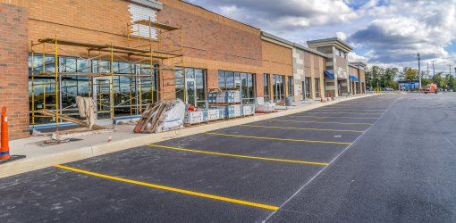 Centro commerciale in costruzione con ponteggi sulla facciata in mattoni, parcheggio asfaltato appena completato e materiali edili sul marciapiede