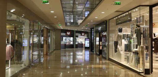 Corridoio interno di un centro commerciale vuoto con negozi di abbigliamento e vetrine illuminate su pavimento in marmo lucido